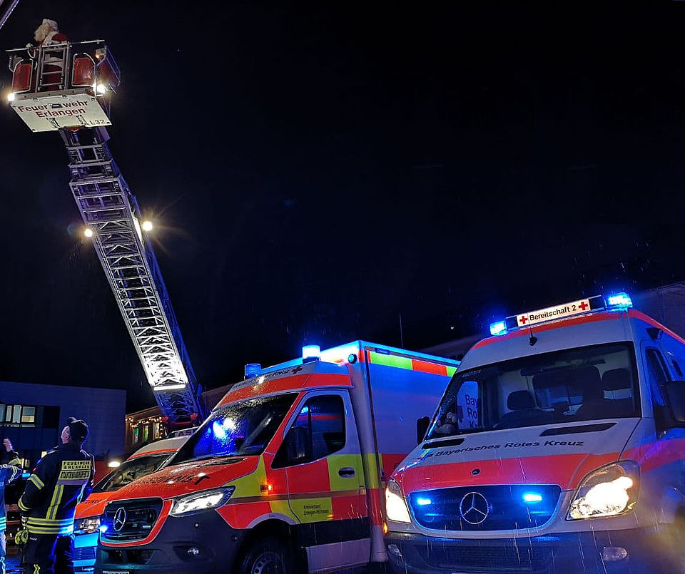 Mehrere Einsatzfahrzeuge stehen mit Blaulicht vor dem Kinderklinik, der Weihnachtsmann winkt von der Drehleiter.