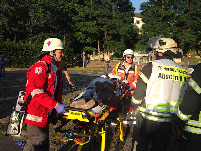 Sanitäter mit einem Verletzten siwie dem Abschnittsleiter der Feuerwehr.